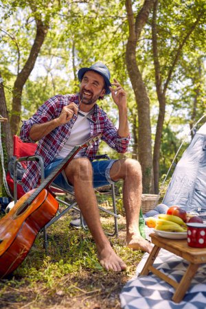 Téléchargez les photos : Homme souriant près d'une tente de camping en vert sur la nature - en image libre de droit