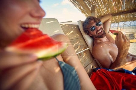 Photo for Happy man and woman on vacation eat watermelon at the beach - Royalty Free Image
