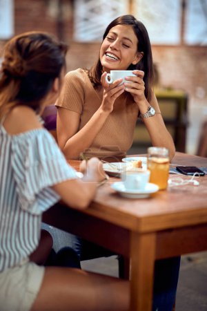 Foto de Dos jóvenes felices disfrutando del café juntos en la cafetería. Charlando y riendo juntos. Estilo de vida, lesión, concepto de pausa para café. - Imagen libre de derechos