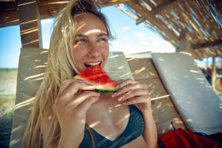 Foto de Hermosa mujer joven disfrutando de pedazo de sandía en la playa. Mujer de vacaciones. Vacaciones, lesiones, concepto de estilo de vida. - Imagen libre de derechos