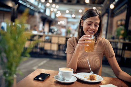 Photo for Beautiful young lady enjoying orange juice. Woman at coffee shop. Student life, young adult, lifestyle. - Royalty Free Image