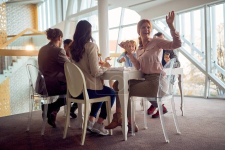 Téléchargez les photos : Les jeunes gens d'affaires sont assis autour de la table pendant une pause déjeuner dans une atmosphère amicale dans le bâtiment de l'entreprise et passer un bon moment tout en mangeant de la pizza. Entreprise, personnes, entreprise - en image libre de droit