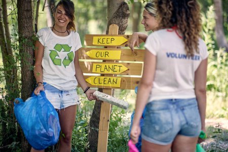 Foto de Equipo de jóvenes voluntarios cuidando la naturaleza, recogiendo basura plástica en la bolsa de basura en el bosque durante la limpieza. - Imagen libre de derechos