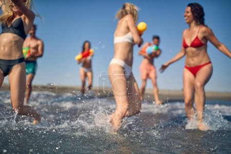 Photo for Blurred shot of group of friends playing with water guns. Young caucasian man and women on summer holiday. Fun, holiday, lifestyle concept. - Royalty Free Image