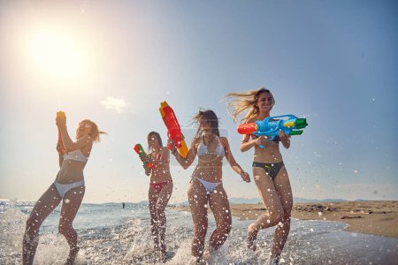 Photo for Group of cheerful friends having a water gun fight on the beach - Royalty Free Image