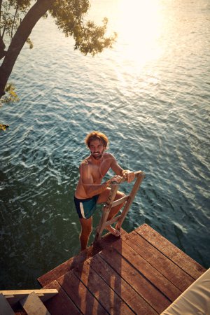 Foto de El joven baja por la escalera para nadar en el río en un hermoso día de verano. Verano, río, vacaciones - Imagen libre de derechos