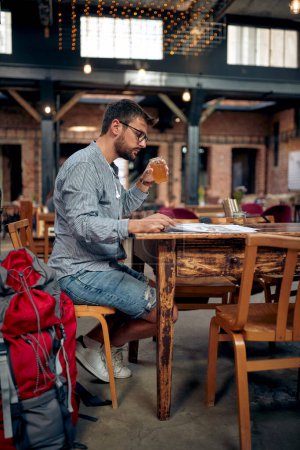 Foto de Joven viajero en una parada de café, disfrutando de la bebida y leyendo el periódico solo en un café. Viajes, estilo de vida, concepto de lesión. - Imagen libre de derechos
