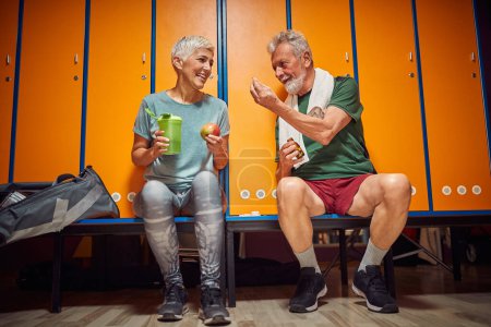Photo for Senior man and woman sitting in dressing room taking pre workout vitamins, lovely senior couple together. Health, lifestyle, togetherness concept. - Royalty Free Image
