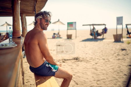 Foto de Un joven está sentado en el bar en la playa y disfruta de la vista en un hermoso día de verano. Verano, playa, mar - Imagen libre de derechos