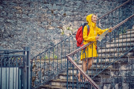 Photo for Traveling in summertime. Joyful young woman with map, in raincoat, happy on her holiday. Backpack, tourism, lifestyle concept. - Royalty Free Image