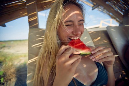 Téléchargez les photos : Femme souriante en bikini bronzer sur une plage et profiter à l'été manger pastèque. - en image libre de droit