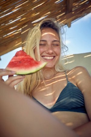 Téléchargez les photos : Femme heureuse en vacances manger pastèque à la plage - en image libre de droit