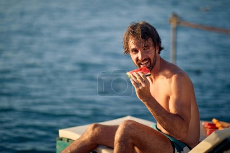 Photo for Smiling man at vacation.handsome Man on dock by the water during the summer sunny day eat watermelon - Royalty Free Image