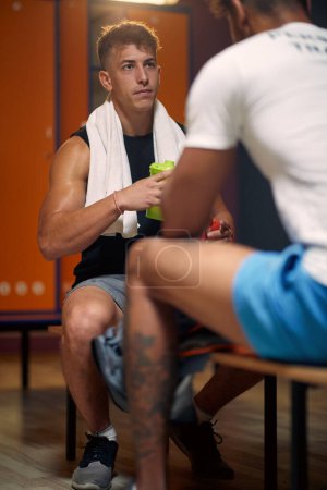 Foto de Entrenador personal con un joven boxeador en el vestidor, sentado en el banco uno frente al otro y hablando. Preparación para el entrenamiento. - Imagen libre de derechos