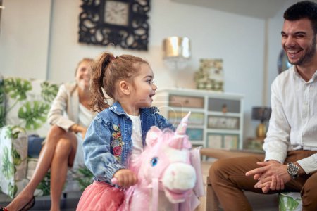 Photo for Young family is captured in a moment of pure joy and happiness. The mother can be seen laughing in the background, while the father stands next to their adorable toddler daughter who is riding a rocking horse toy. The trio is having a great time as t - Royalty Free Image