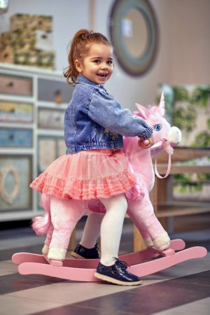 Foto de Niña feliz y alegre sentada en un unicornio rockero. - Imagen libre de derechos