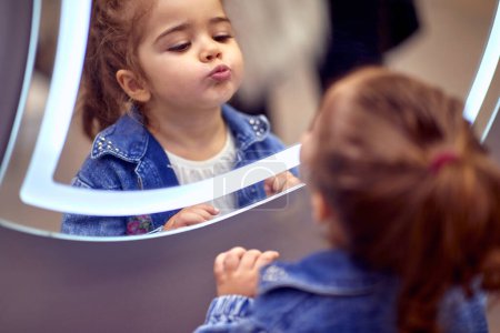 Photo for Little girl who is playing with her reflection in the mirror. - Royalty Free Image