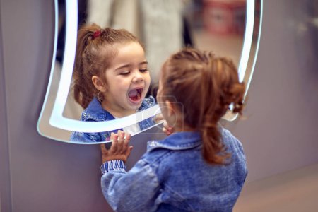 Téléchargez les photos : Petite fille mignonne qui joue avec son reflet dans le miroir. - en image libre de droit