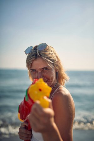 Foto de Mujer joven apuntando con pistola de agua. Mujer atractiva feliz en la playa en vacaciones de verano. Vacaciones, diversión, concepto de estilo de vida. - Imagen libre de derechos