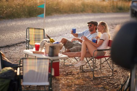 Téléchargez les photos : Un jeune couple assis au camping par une belle journée ensoleillée en pleine nature et profitant de la vue et de la boisson. Relation, amour, camping, nature - en image libre de droit