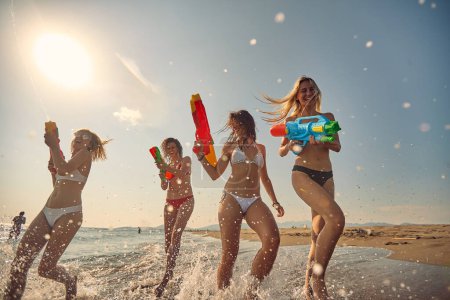 Téléchargez les photos : Jeunes belles femmes avec des pistolets à eau courant sur le rivage. Vacances d'été. Ensemble, amusement, vacances, concept de style de vie. - en image libre de droit