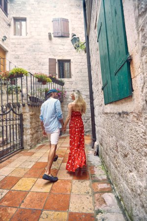 Photo for Lovely date. Couple on walk. Woman in red sultry summer dress and stylish handsome man holding hands. Date, honeymoon, love, holiday concept. - Royalty Free Image