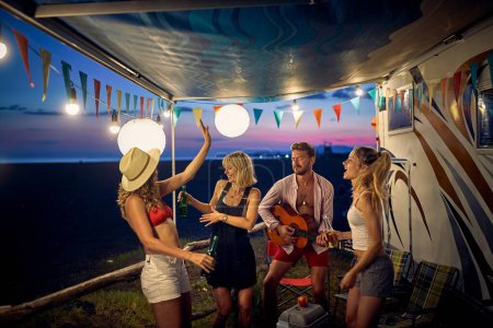 Photo for A group of friends having a good time with drink and music on a beautiful night in the camp during a vacation in the nature. Vacation, friendship, camping, nature - Royalty Free Image