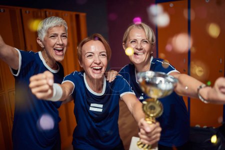Photo for Team of mature women and young trainer in sportswaer uniform winning golden cup, feeling victorious. - Royalty Free Image