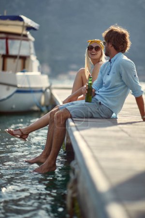 Photo for Young couple sitting on the dock and enjoys by the lake - Royalty Free Image