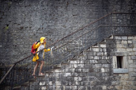 Foto de Joven turista en impermeable subiendo escaleras mirando el mapa, sintiéndose victorioso. Arreciendo en su destino. Viajes, ciudad, concepto de estilo de vida. - Imagen libre de derechos