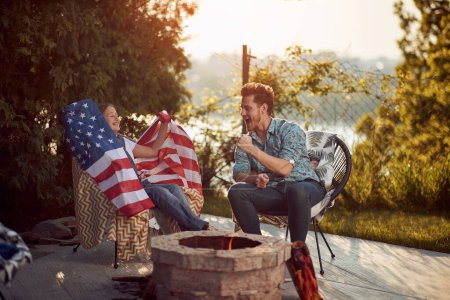 Foto de Celebración familiar del Día de la Independencia. En el ambiente de calidez y alegría, la hija muestra orgullosamente una bandera americana desplegada, que simboliza su orgullo y patriotismo estadounidenses profundamente arraigados. - Imagen libre de derechos
