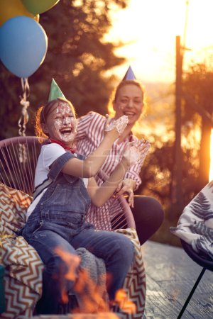 Photo for Mother and daughter duo celebrating the daughter's birthday. Laughter fills the air as they delight in the daughter's face covered in sweet, creamy frosting from the birthday cake. - Royalty Free Image