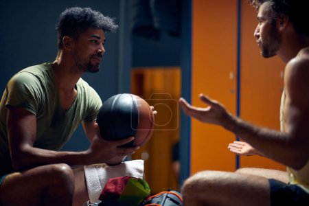 Téléchargez les photos : Hommes sportifs dans la salle de gym dressing avec ballon de basket, après la conversation d'entraînement, profiter de l'autre compagnie. Sport, concept lifestyle. - en image libre de droit