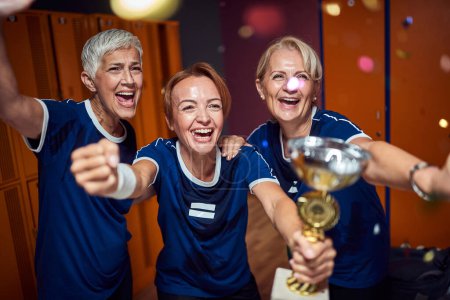 Photo for Lovely team of senior and young women celebration win with golden cup together in locker room. Female soccer team win. - Royalty Free Image
