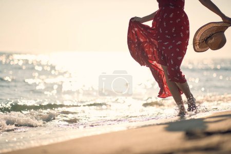 Foto de Mujer en vestido rojo caminando en la playa de arena - Imagen libre de derechos