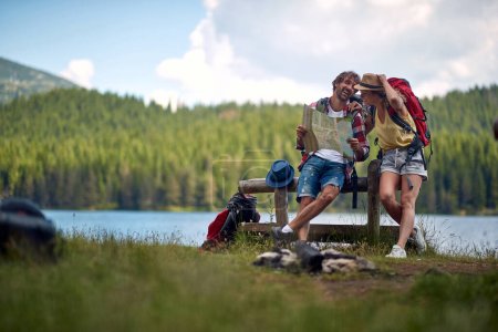 Téléchargez les photos : Couple souriant pendant le voyage naviguer avec la carte et planifier d'autres sentiers de randonnée - en image libre de droit