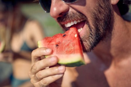 Téléchargez les photos : Gros plan de l'homme mangeant des fruits de pastèque sur la plage. Couple en vacances. Vacances, convivialité, concept de style de vie. - en image libre de droit