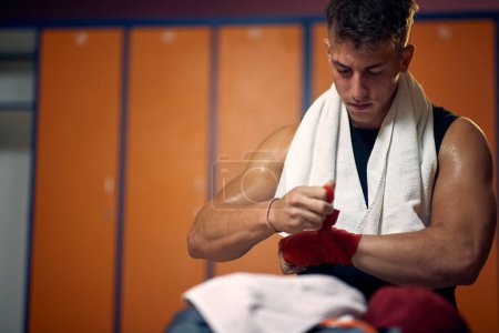 Photo for Wide horizontal shot of young sweaty man taking red protective tape of his hands after boxing workout. Health, sports, active lifestyle concept. - Royalty Free Image