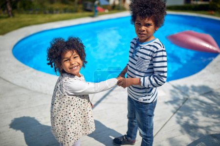 Foto de Hermanos afroamericanos mientras disfrutan de un momento lúdico junto a la piscina. Con un sentido del humor compartido, su risa alegre llena el aire, haciéndose eco del vínculo profundo que comparten. - Imagen libre de derechos