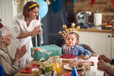 Téléchargez les photos : Une petite fille, remplie de joie et d'excitation, souffle les bougies sur son gâteau d'anniversaire, entourée de sa mère aimante, de sa grand-mère aimante et de son fier grand-père. - en image libre de droit