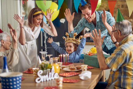 Photo for Little girl joyfully celebrates her birthday surrounded by her parents,grandparents,and a decorated birthday cake.Everyone raises their hands in the air,embracing the joyous moment together. - Royalty Free Image