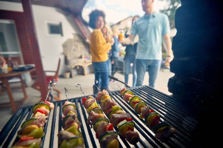 Photo for Close-up view of a sizzling grill. The grill grates showcase perfectly cooked food.In the background, a group of people can be seen gathered around. - Royalty Free Image