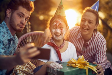 Photo for Close up portrait shot of beautiful birthday girl with cake on her face, celebrating birthday with mom and dad, posing for a picture. Celebration, lifestyle concept. - Royalty Free Image