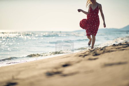 Foto de Una joven está disfrutando del viento mientras camina por la playa en un hermoso día de verano. Verano, playa, mar, vacaciones - Imagen libre de derechos