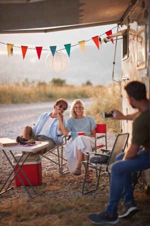 Photo for Man taking a photo of a couple. Sitting outdoors in front of camper rv. Fun, togetherness, love concept. - Royalty Free Image