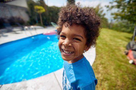 Foto de Pura alegría y exuberancia de un chico afroamericano junto a la piscina. Con el sol brillando intensamente, su risa infecciosa llena el aire, creando una atmósfera de felicidad desenfrenada. - Imagen libre de derechos