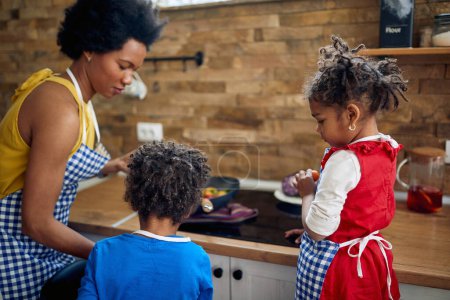 Photo for Afro-American family kitchen as the mother lovingly prepares a meal together with her delightful young son and daughter. - Royalty Free Image