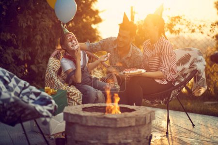 Photo for Joyful birthday girl smearing her face with cake, enjoying birthday celebration with her family outdoors in nature in a cozy cottage by a fireplace. Lifestyle, celebration concept. - Royalty Free Image
