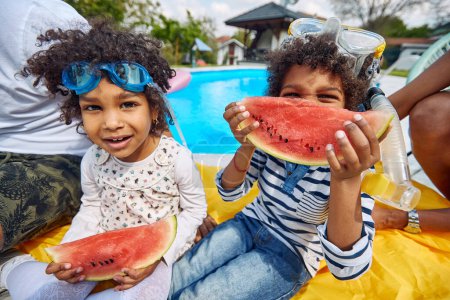 Téléchargez les photos : Moments estivaux d'une famille afro-américaine au bord de la piscine. Les parents, avec leurs enfants, un garçon et une fille, se réunissent pour savourer les délices d'un festin rafraîchissant de pastèque. - en image libre de droit