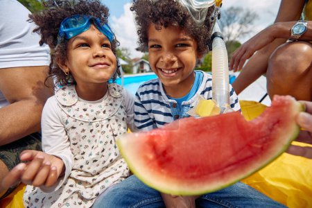 Photo for Summer moments of an Afro-American family by the poolside. The parents, along with their children, a boy and a girl, come together to savor the delights of a refreshing watermelon feast. - Royalty Free Image